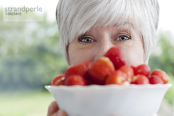 Gesicht einer Frau hinter einer Schüssel mit frischen Erdbeeren