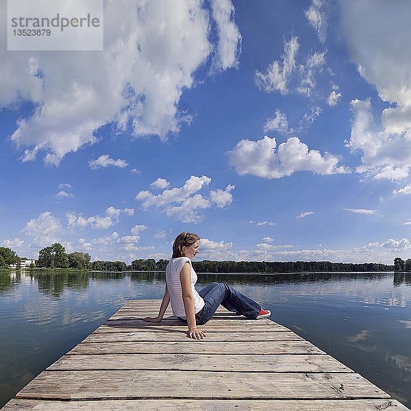 Mädchen entspannt sich auf einem Steg eines Baggersees mit reflektiertem Wolkenhimmel  Ingolstadt  Bayern  Deutschland  Europa