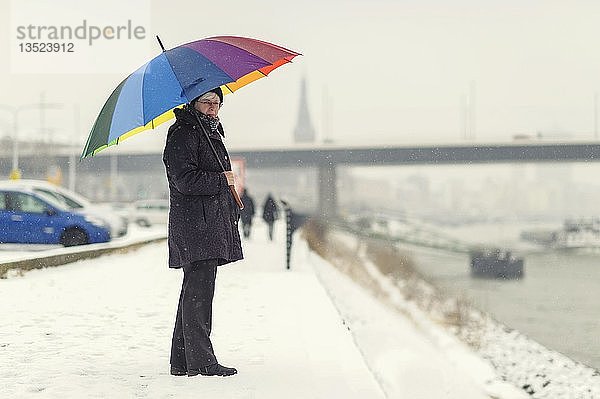 Frau steht mit einem bunten Regenschirm im Winter am Rheinufer  Düsseldorf  Rheinland  Nordrhein-Westfalen  Deutschland  Europa