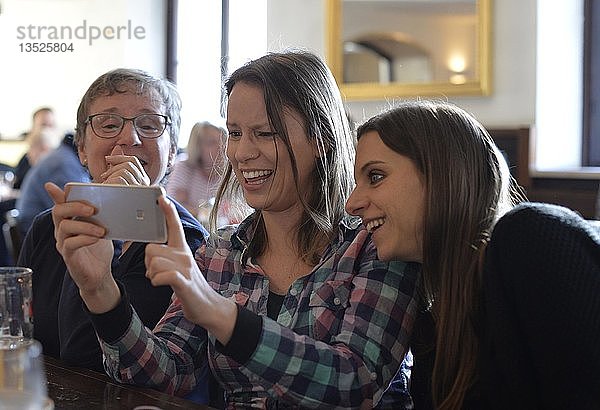 Junge Frauen und ältere Frauen betrachten Smartphone  Lachen  Porträt  Café  Stuttgart  Baden-Württemberg  Deutschland  Europa