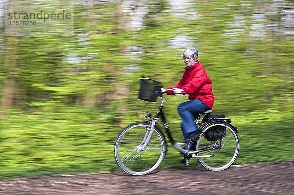 Ältere Frau in roter Jacke fährt mit dem Fahrrad durch den Wald