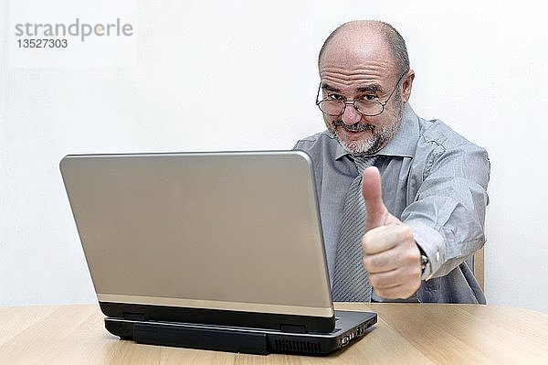 Mann an seinem Laptop  der die Daumen nach oben streckt