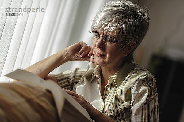Ältere Frau sitzt am Fenster und liest ein Buch  Nordrhein-Westfalen  Deutschland  Europa
