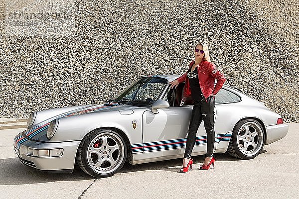 Junge Frau mit langen blonden Haaren posiert mit Porsche 911 Carrera 4