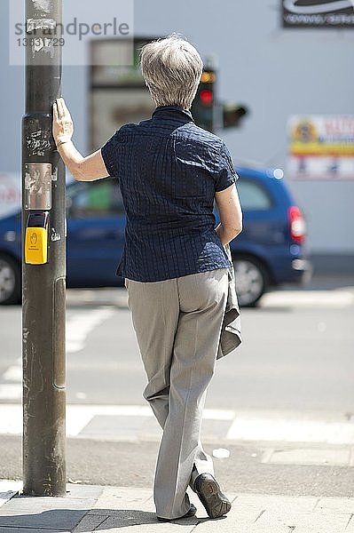 Frau  50+  wartet auf das grüne Licht einer Ampel an einer Kreuzung