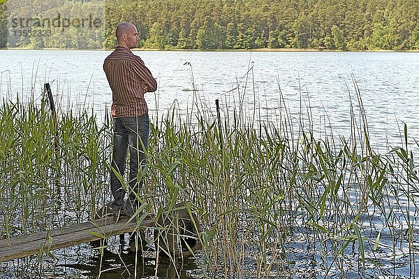 Junger Mann steht am Ufer eines Sees