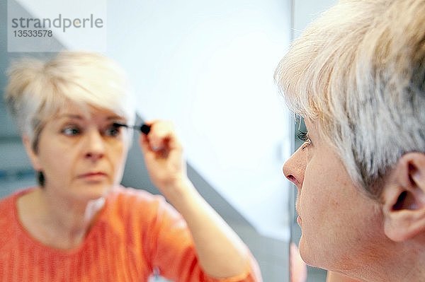 Frauen  50+  schauen in den Spiegel  während sie sich schminken