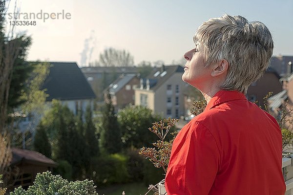 Frau in roter Bluse steht auf einem Balkon und genießt die Sonne  Grevenbroich  Nordrhein-Westfalen  Deutschland  Europa