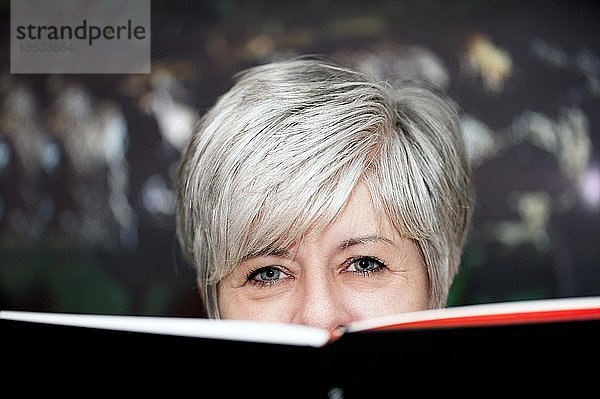 Grauhaarige Frau schaut über den Rand eines Buches