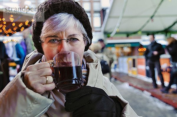 Frau  50+  trinkt Glühwein auf dem Weihnachtsmarkt