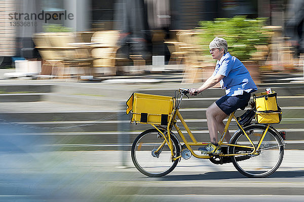 Briefträgerin fährt mit dem Fahrrad durch die Stadt  Grevenbroich  Nordrhein-Westfalen  Deutschland  Europa