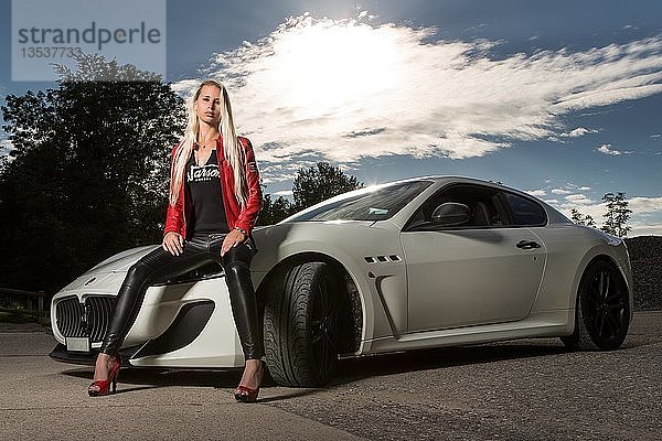 Junge Frau mit langen blonden Haaren posiert mit weißem Maserati Gran Turismo MC Stradale