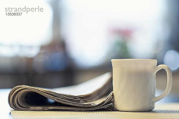 Eine Tasse Kaffee und eine Zeitung liegen auf einem Küchentisch  Deutschland  Europa