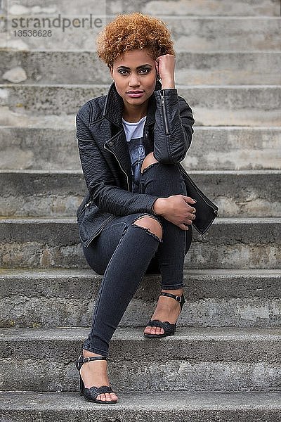 Junge dunkle Frau  die auf einer Steintreppe sitzt  Mode  Porträt