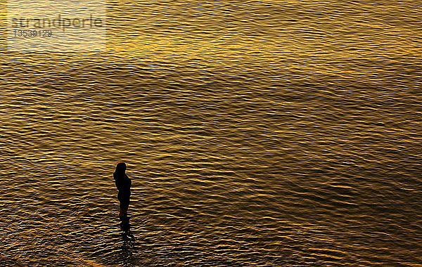 Eine junge Frau in Gedanken versunken an der Ostsee bei Sonnenuntergang