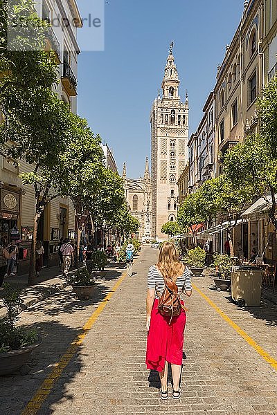 Frau mit rotem Kleid auf der Straße  mit Blick auf La Giralda  Glockenturm der Kathedrale von Sevilla  Catedral de Santa Maria de la Sede  Sevilla  Andalusien  Spanien  Europa