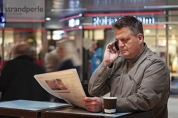 Mann mit Mobiltelefon  der eine Zeitung liest  Düsseldorf  Nordrhein-Westfalen  Deutschland  Europa