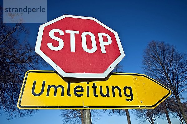 Stoppschild und deutsches Umleitungsschild vor blauem Himmel