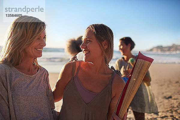 Glückliche Mutter und Tochter mit Yogamatte am sonnigen Strand während eines Yoga-Retreats