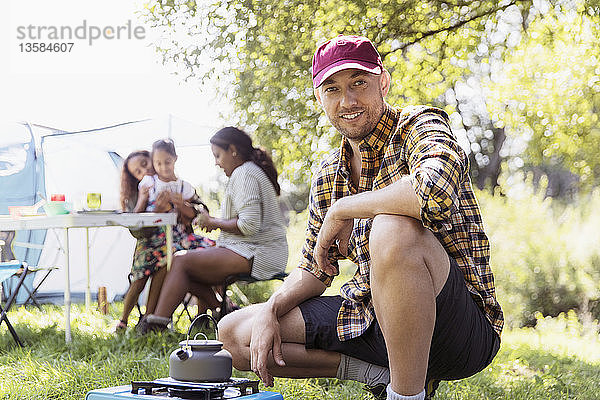 Porträt eines selbstbewussten Mannes  der eine Teekanne auf einem Campingkocher auf einem sonnigen Campingplatz erhitzt