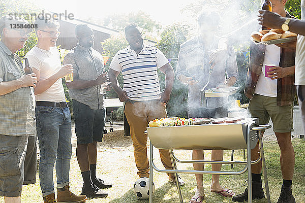 Männliche Freunde trinken Bier und grillen im sonnigen Sommergarten