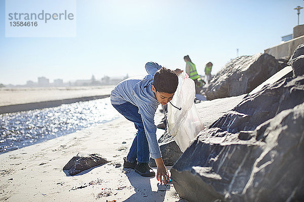 Freiwilliger Junge sammelt Müll am sonnigen Strand auf