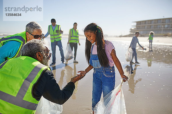 Großeltern und Enkelin beseitigen freiwillig Müll am sonnigen  nassen Sandstrand