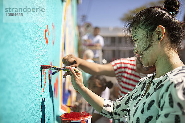 Lächelnde weibliche Freiwillige malt ein Wandbild an einer sonnigen Wand