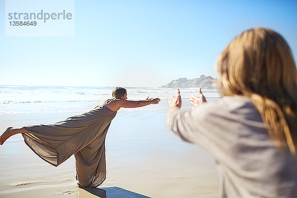 Frau übt Krieger 3 Pose am sonnigen Strand während Yoga-Retreat
