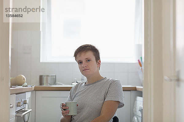 Porträt einer selbstbewussten jungen Frau im Rollstuhl  die in einer Wohnküche Kaffee trinkt