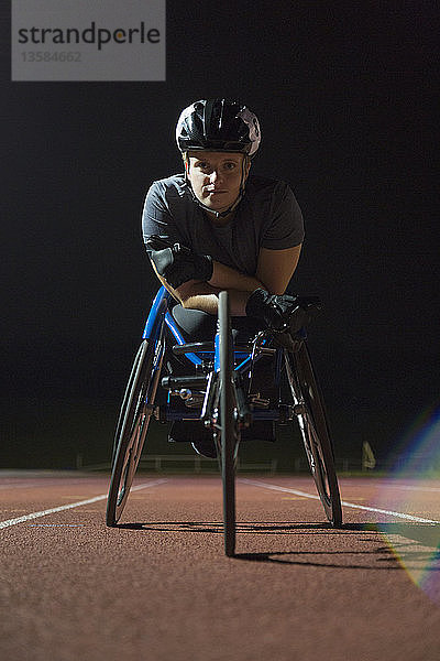 Porträt einer entschlossenen  zähen jungen querschnittsgelähmten Athletin  die nachts auf einer Sportbahn für ein Rollstuhlrennen trainiert