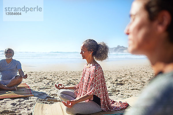 Gelassene ältere Frau meditiert am sonnigen Strand während eines Yoga-Retreats