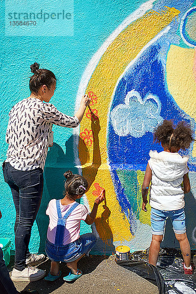Mutter und Tochter malen als Freiwillige ein lebendiges Wandgemälde an eine sonnige Wand