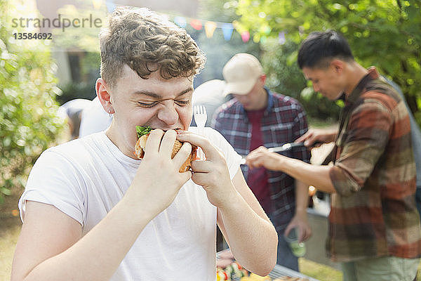 Hungriger Teenager isst Hamburger beim Grillen im Hinterhof