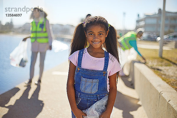 Porträt eines lächelnden Mädchens  das als freiwillige Helferin an der sonnigen Strandpromenade Müll aufräumt