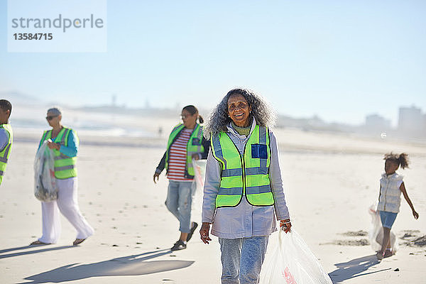 Porträt einer selbstbewussten älteren Frau  die als Freiwillige an einem sonnigen Strand Müll aufräumt