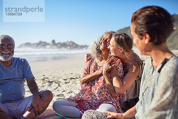 Glückliche Frauen umarmen sich am sonnigen Strand während eines Yoga-Retreats
