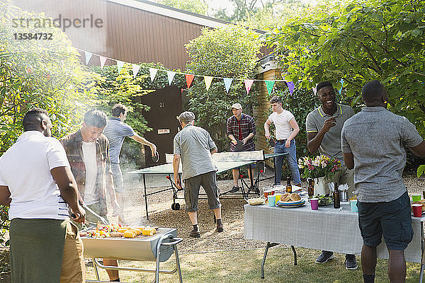 Männliche Freunde spielen Tischtennis und genießen das Grillen im Hinterhof