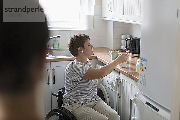 Junge Frau im Rollstuhl bereitet Tee in der Wohnküche zu