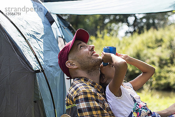 Neugieriger Vater und Tochter beobachten Vögel mit einem Fernglas auf einem sonnigen Campingplatz