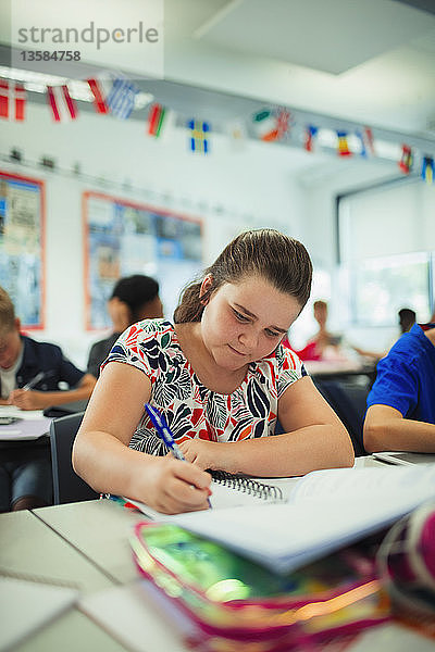 Konzentrierte Junior High School Schülerin macht Hausaufgaben am Schreibtisch im Klassenzimmer
