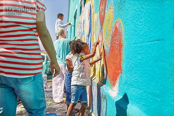 Freiwilliges Mädchen malt ein lebendiges Wandgemälde an eine sonnige Wand