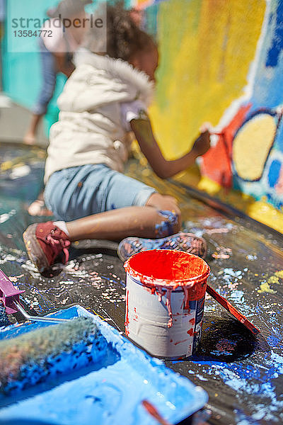Mädchen malt Wandbild hinter Farbdose