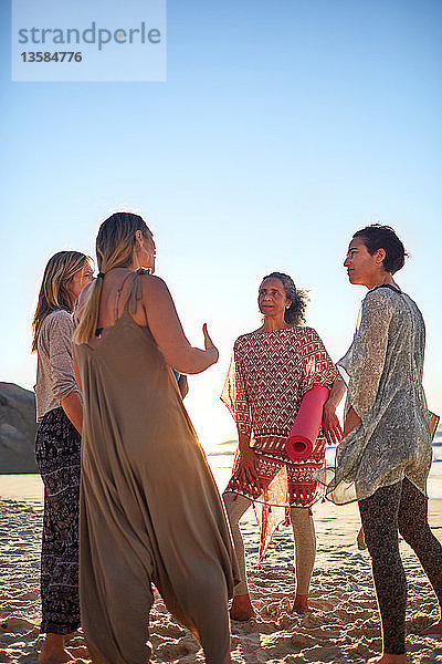 Frauen mit Yogamatten im Gespräch am sonnigen Strand während eines Yoga-Retreats