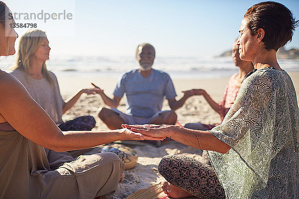 Gelassene Menschen meditieren im Kreis am sonnigen Strand während eines Yoga-Retreats