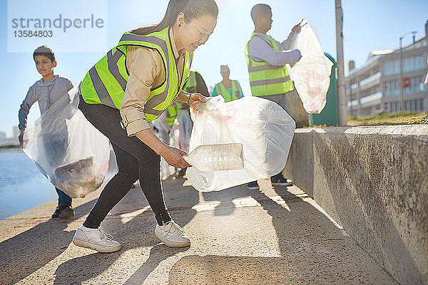 Freiwillige Frau sammelt Plastikmüll an der sonnigen Strandpromenade auf
