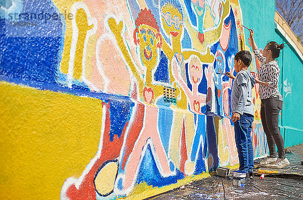 Mutter und Sohn malen als Freiwillige ein lebendiges Wandgemälde an eine sonnige Wand