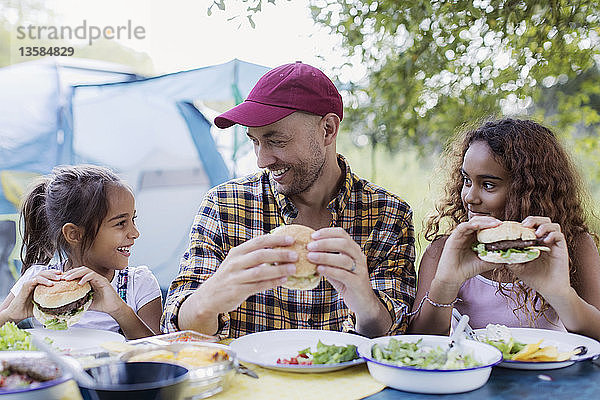 Vater und Töchter genießen einen Hamburger vom Grill auf dem Campingplatz