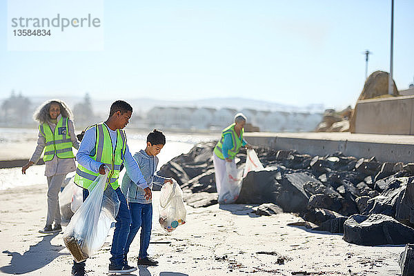 Vater und Sohn beseitigen als Freiwillige den Müll am sonnigen Strand