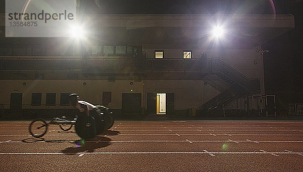 Männlicher querschnittsgelähmter Sportler trainiert für ein Rollstuhlrennen auf einer Sportbahn bei Nacht